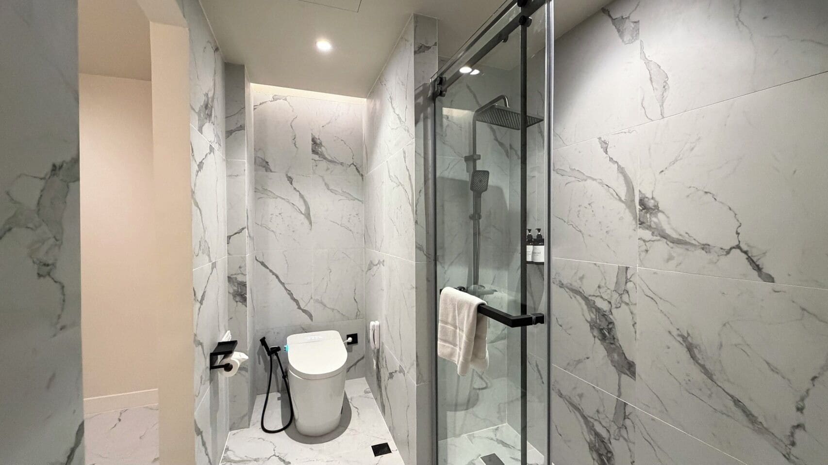 A modern bathroom with a glass-enclosed shower, marble walls, and a toilet.