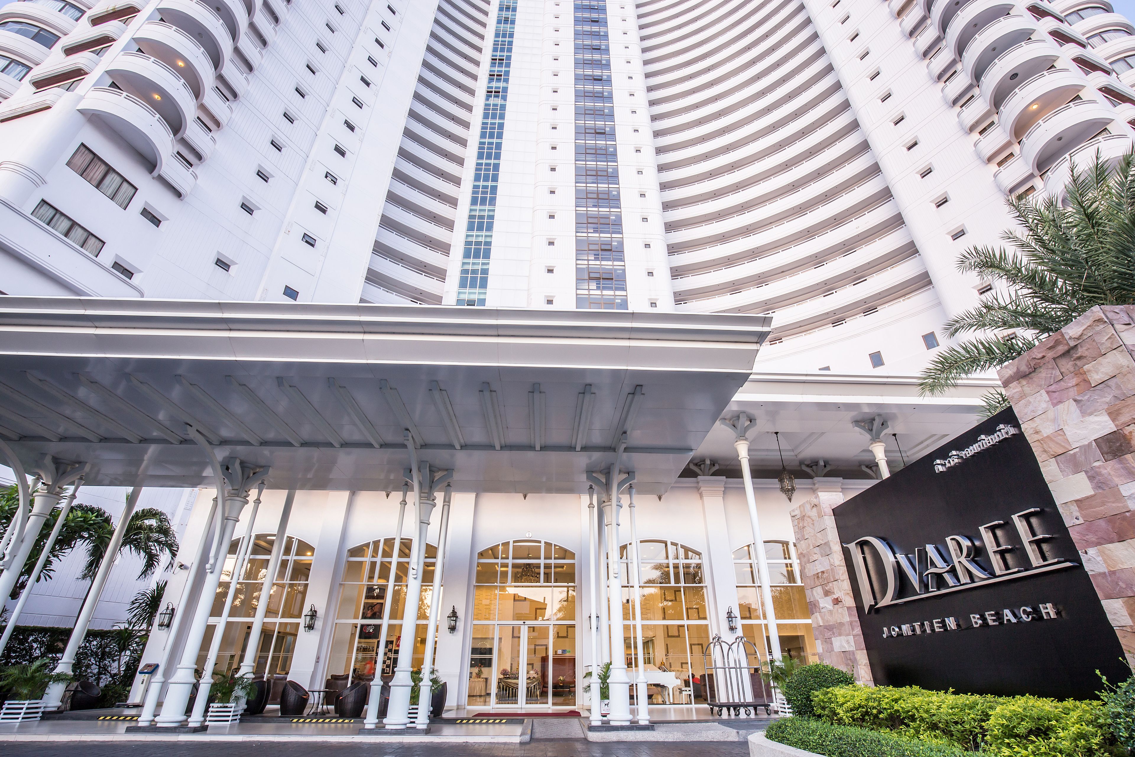 A high-rise hotel with a modern design, featuring a prominent entrance with a covered walkway and a sign that reads "Dvarge Johmten Beach".