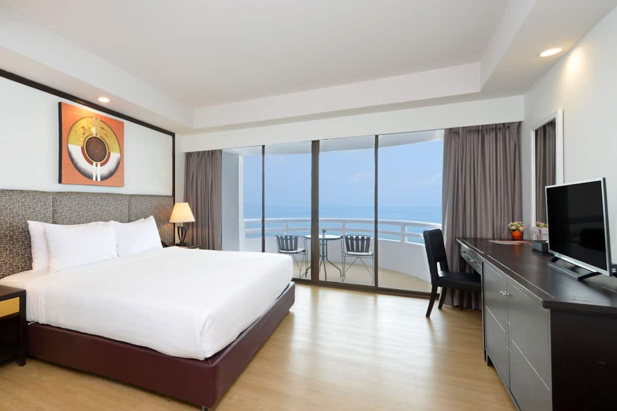 Une chambre d’hôtel dotée d’un grand lit, de deux lampes de chevet, d’un téléviseur à écran plat, d’un bureau et d’un balcon avec vue sur la mer.
