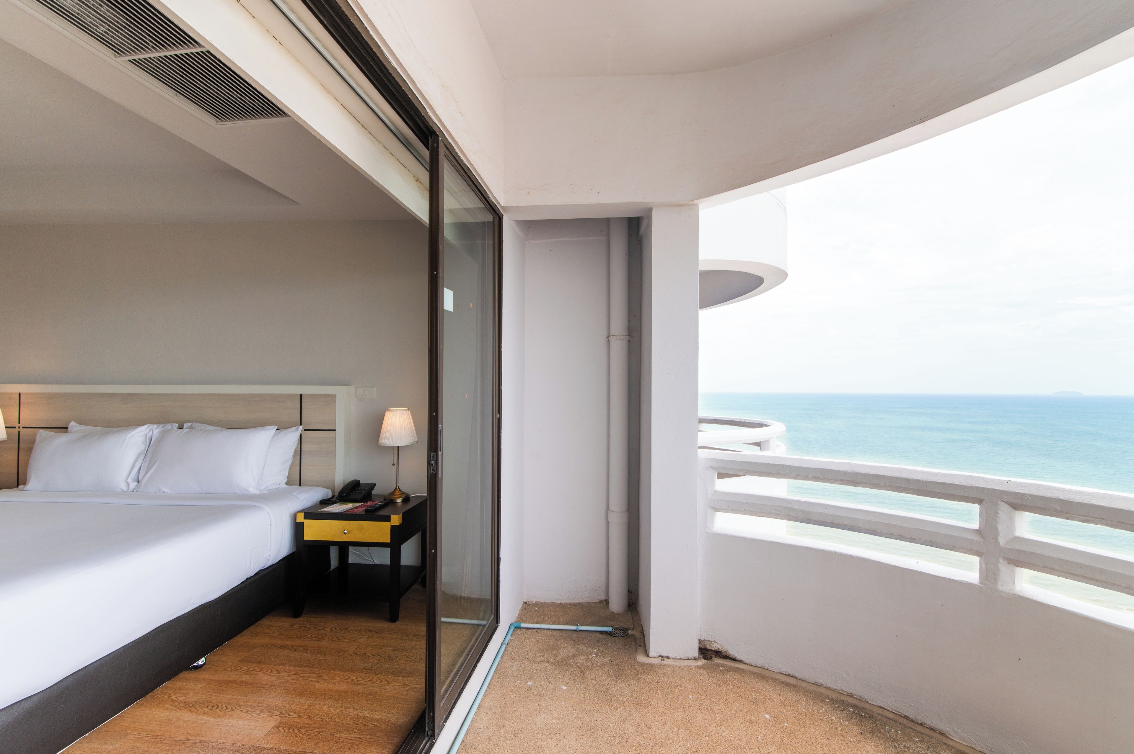 A hotel room with a bed, bedside table, lamp, and a view of the sea.