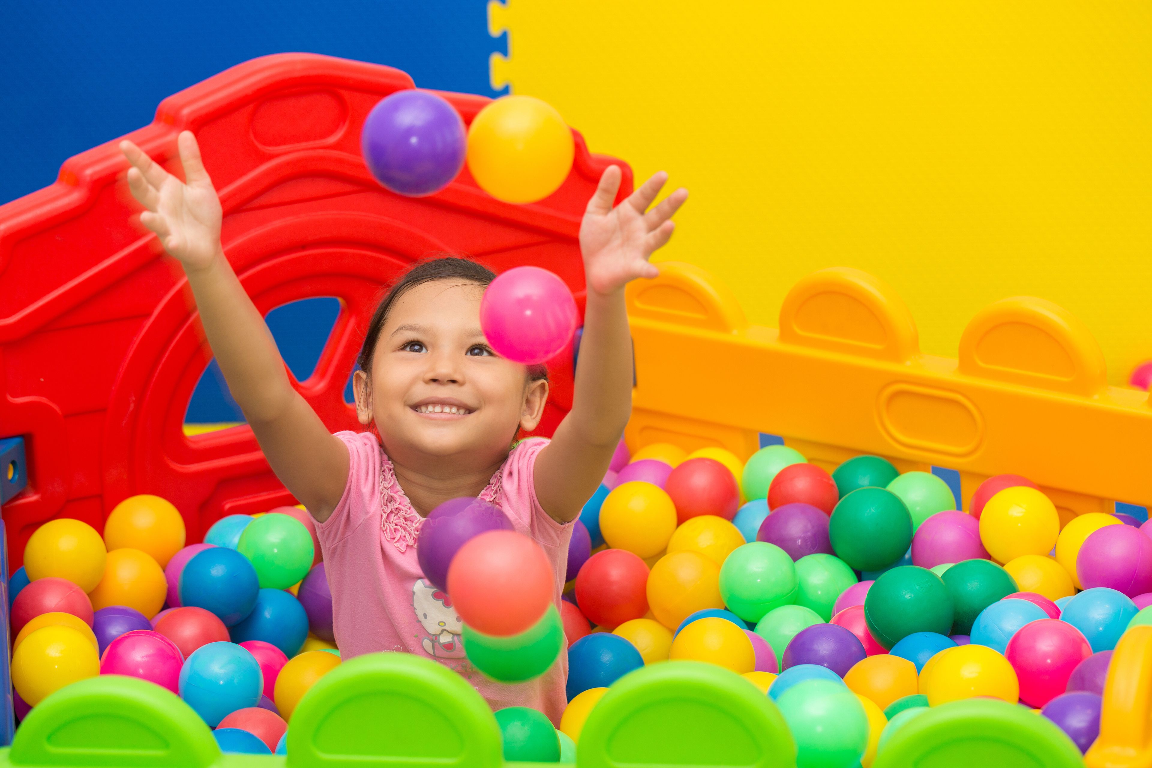A child playing in a ball pit with colorful balls and a red play structure.
