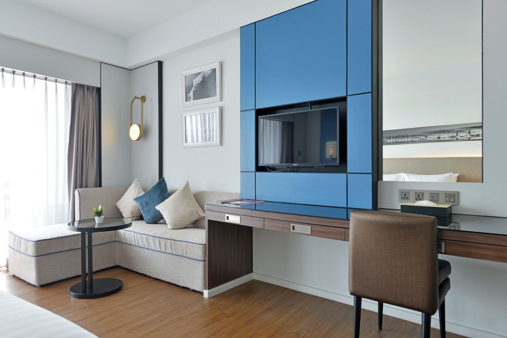 A modern hotel room with a sofa, a small round table, a TV, and a chair.