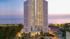 A high-rise hotel with multiple floors, a central entrance, and a parking area. - D Varee Jomtien Beach (Pattaya)