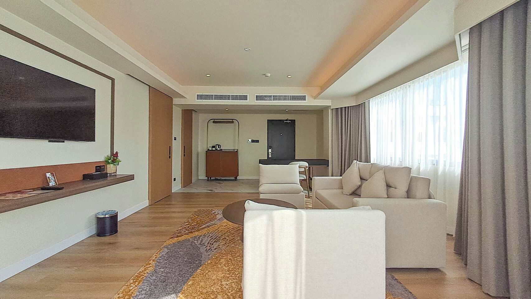 A modern living room with a flat-screen TV, a sofa, a coffee table, and a dining area in the background.