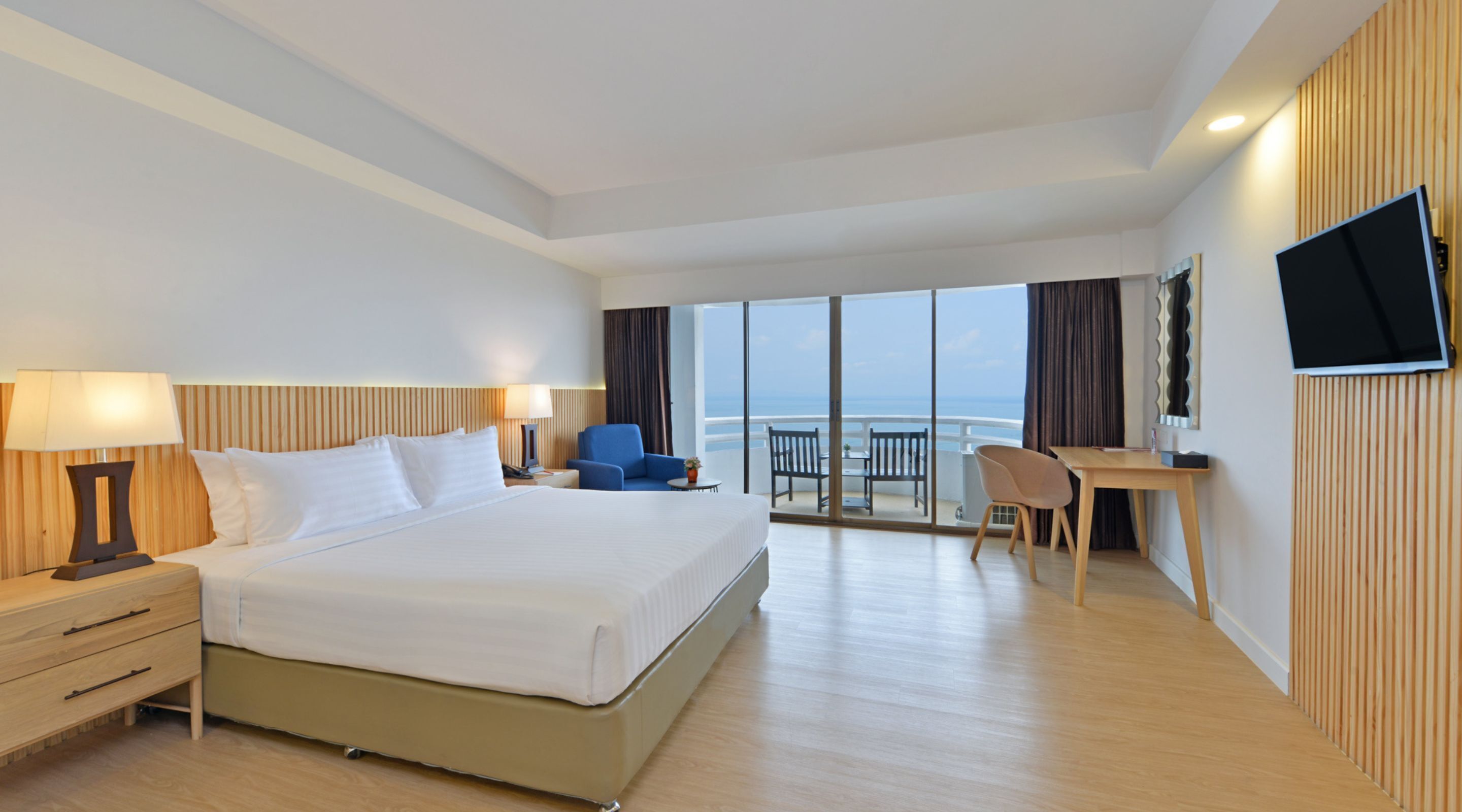 Une chambre d’hôtel avec un grand lit, un bureau, une chaise, une télévision et un balcon avec vue sur la mer.