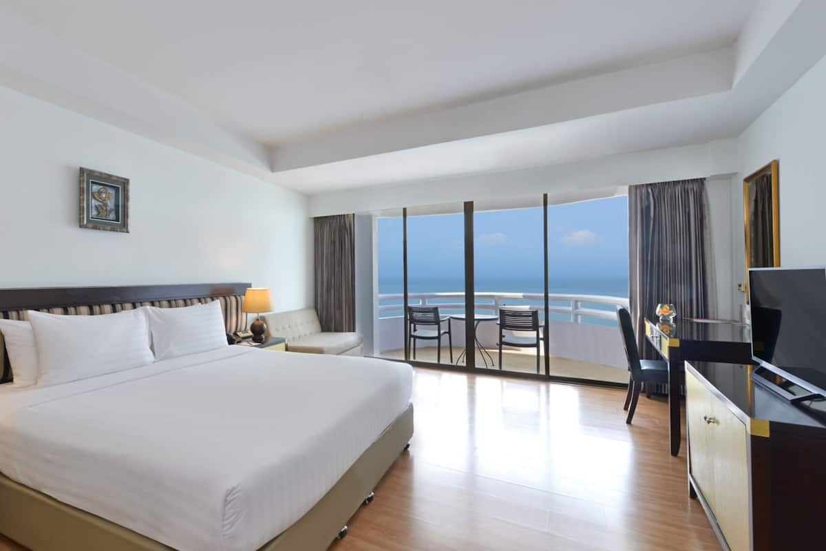 Une chambre d’hôtel avec un grand lit, un bureau avec une télévision et un balcon offrant une vue sur la mer.