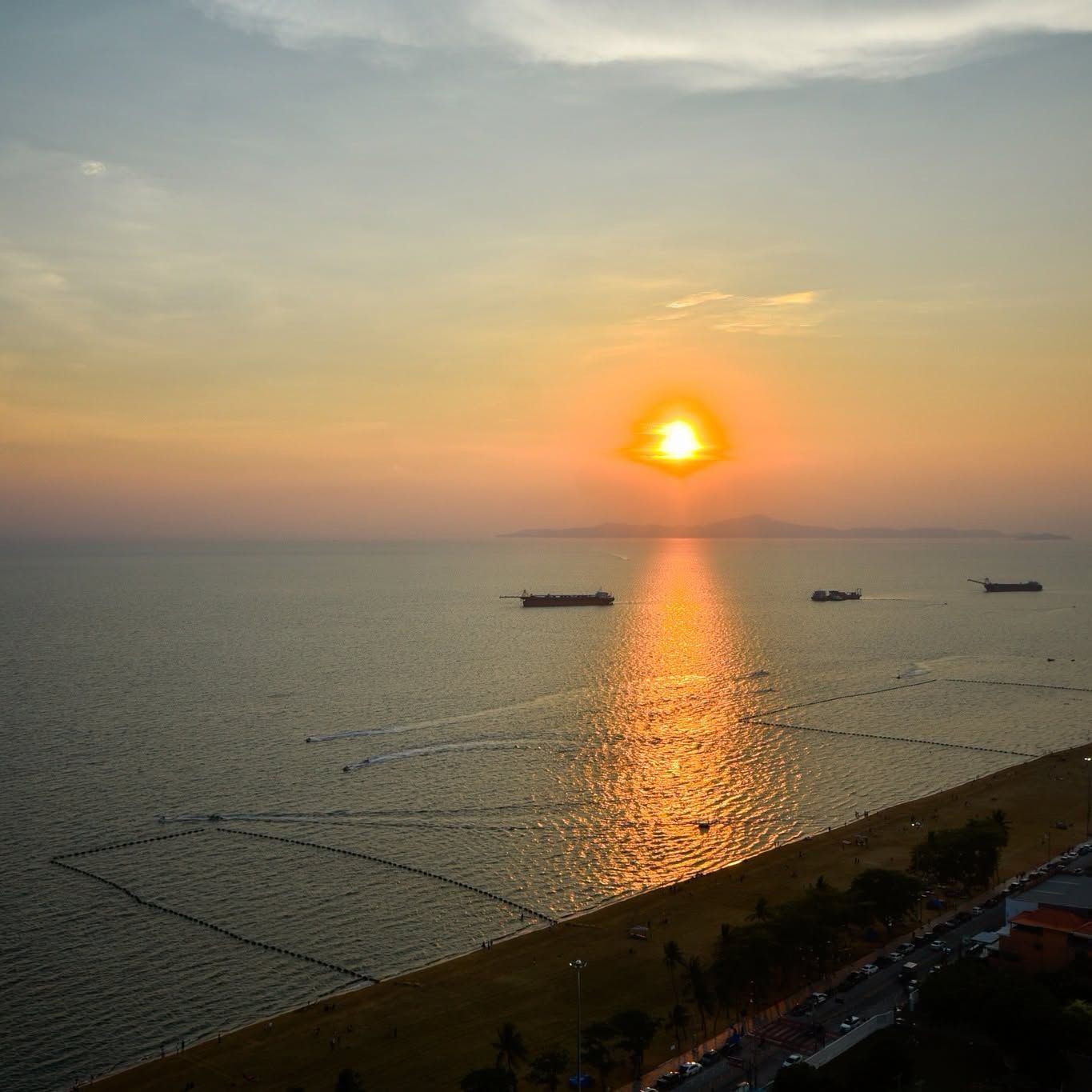 A sunset over a calm sea with ships, a beach, and a clear horizon.
