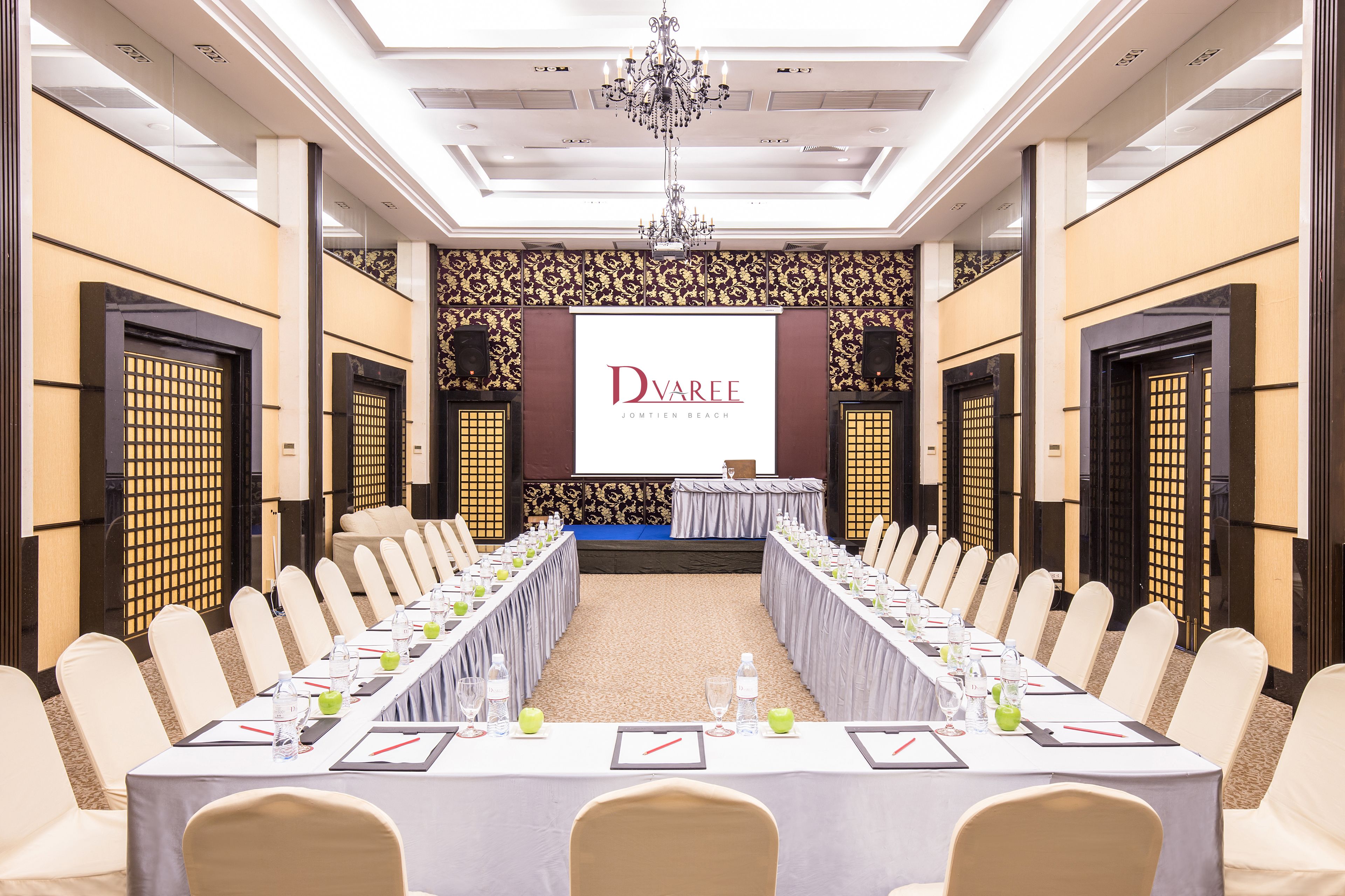 A conference room with a long table, chairs, and a screen displaying 'Dvarree Jomtien Beach'.
