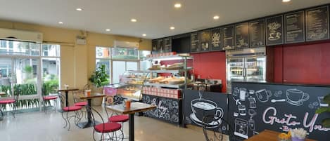 Una cafetería con un menú en pizarra, sillas rojas y una máquina de café.