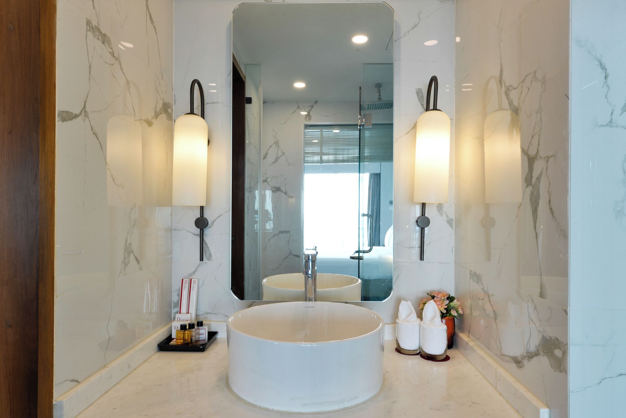 Une salle de bain moderne avec un grand lavabo rond, des murs en marbre et deux appliques murales.