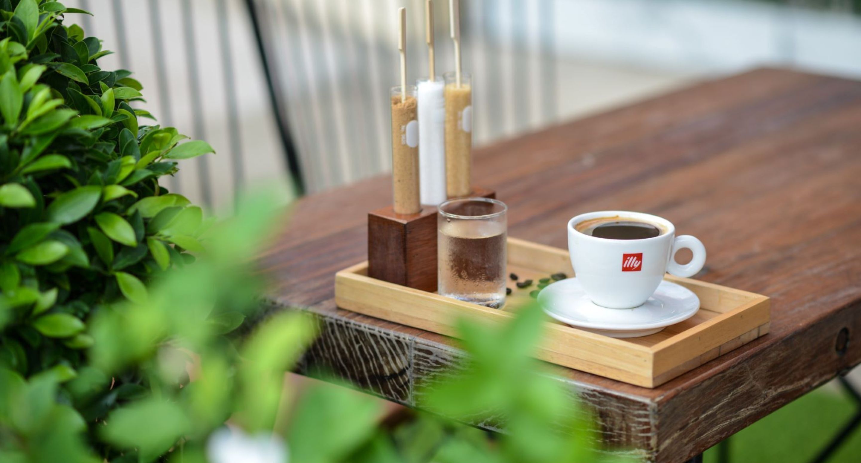 A wooden table with a white cup labeled "illy" and a glass of water.