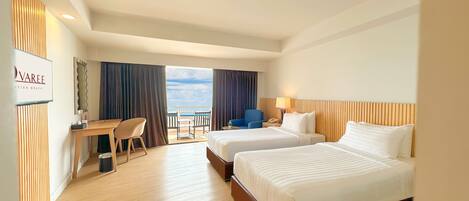 A hotel room with two beds, a desk, a chair, and a view of the beach.