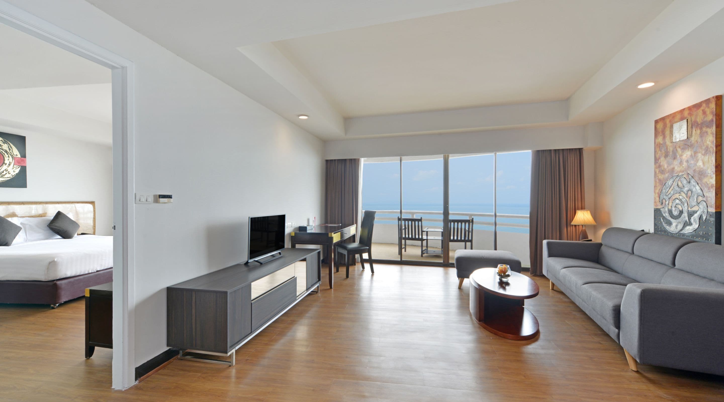 A modern hotel room with a bed, a TV, a desk, a sofa, and a balcony with a view of the sea.
