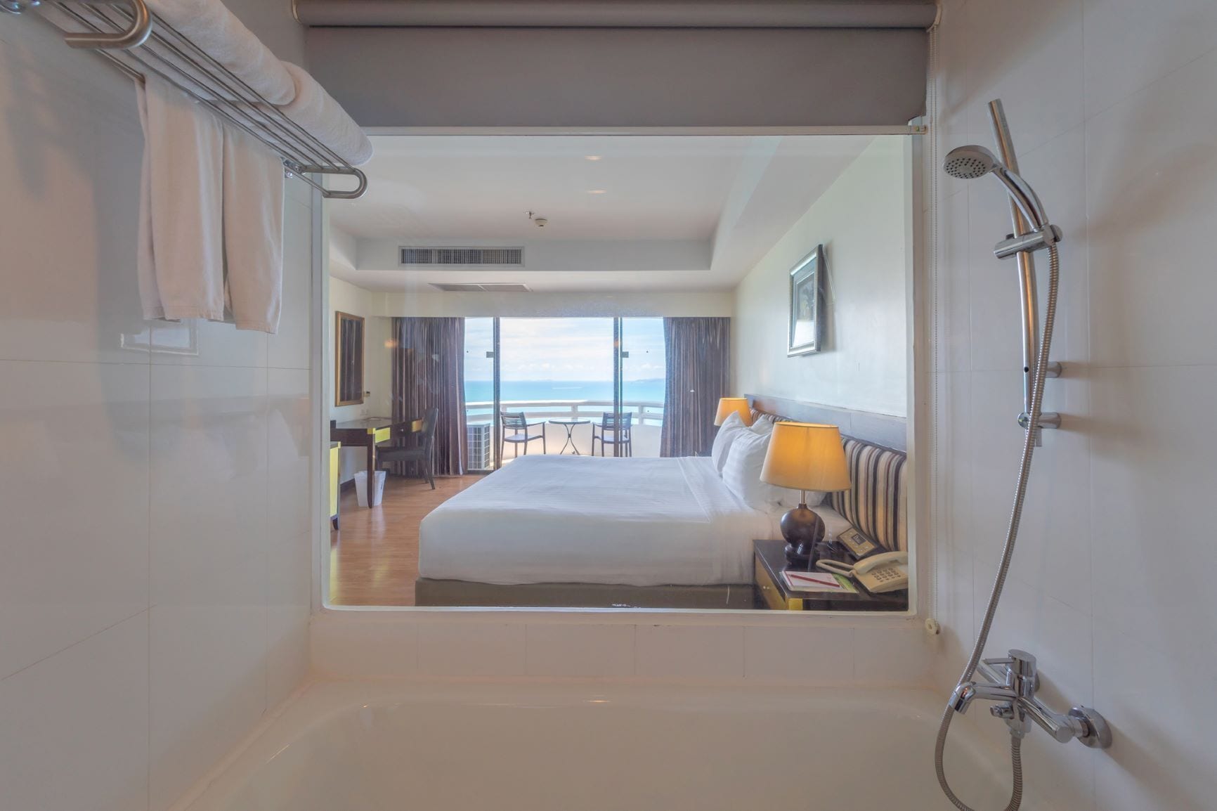 Une chambre d’hôtel dotée d’un grand lit, d’un bureau, d’une chaise, d’une table, d’un balcon avec vue sur la mer et d’un espace douche.