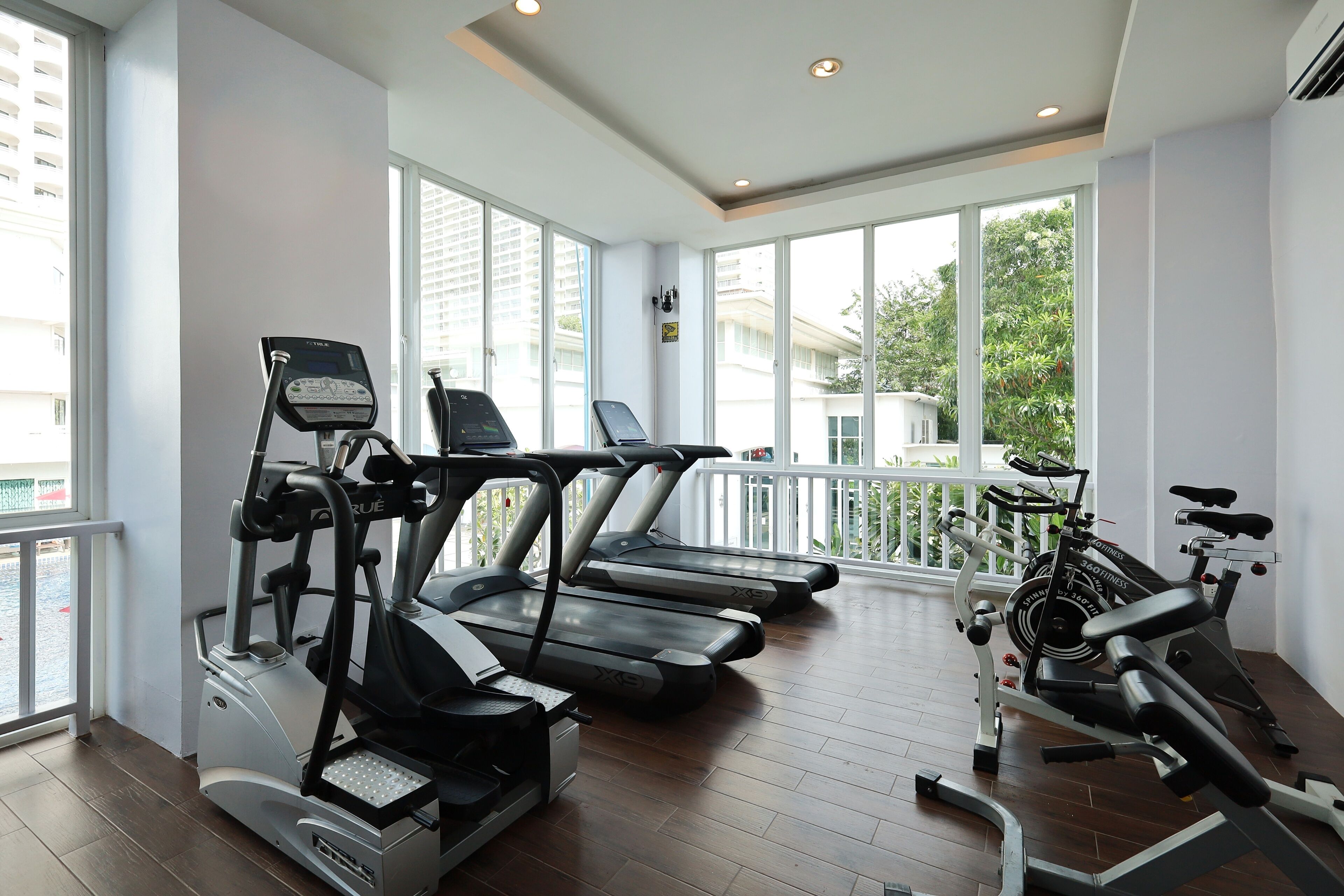 A gym with treadmills, elliptical machines, and a rowing machine, large windows, and a balcony.