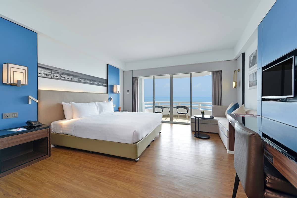 Une chambre d’hôtel avec un grand lit, un bureau, une télévision et un balcon donnant sur la mer.