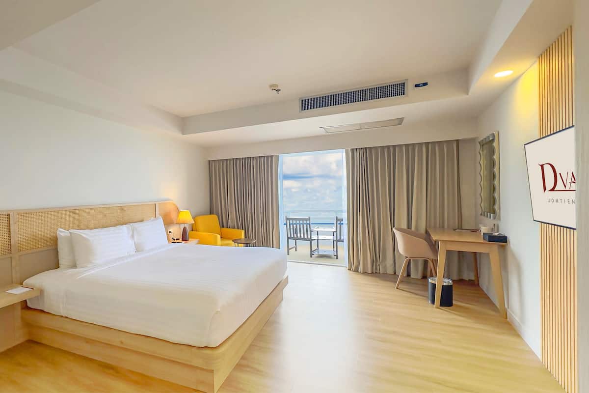 Une chambre d’hôtel avec un grand lit, un bureau, une chaise, une petite table et une vue sur la mer.