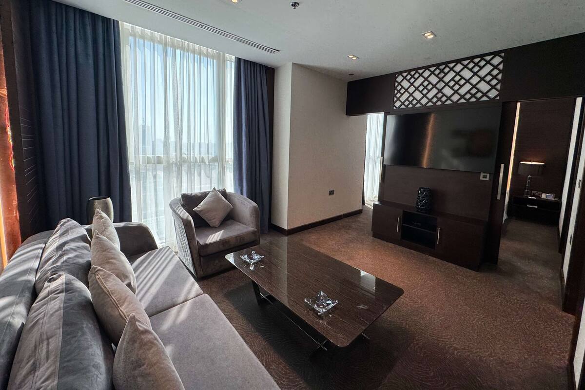 A modern hotel room with a sofa, a coffee table, a TV, and a kitchen area.