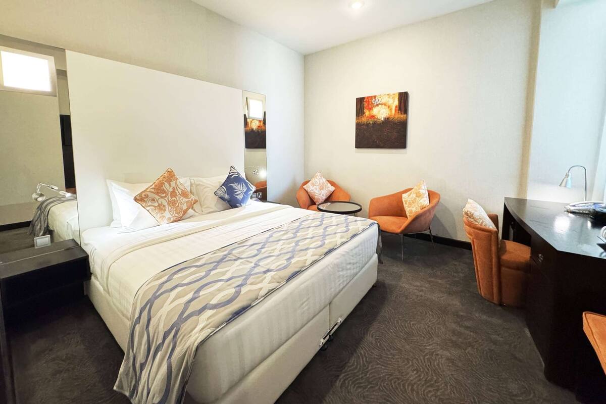 A hotel room with a bed, a desk, a chair, a mirror, and a painting on the wall.