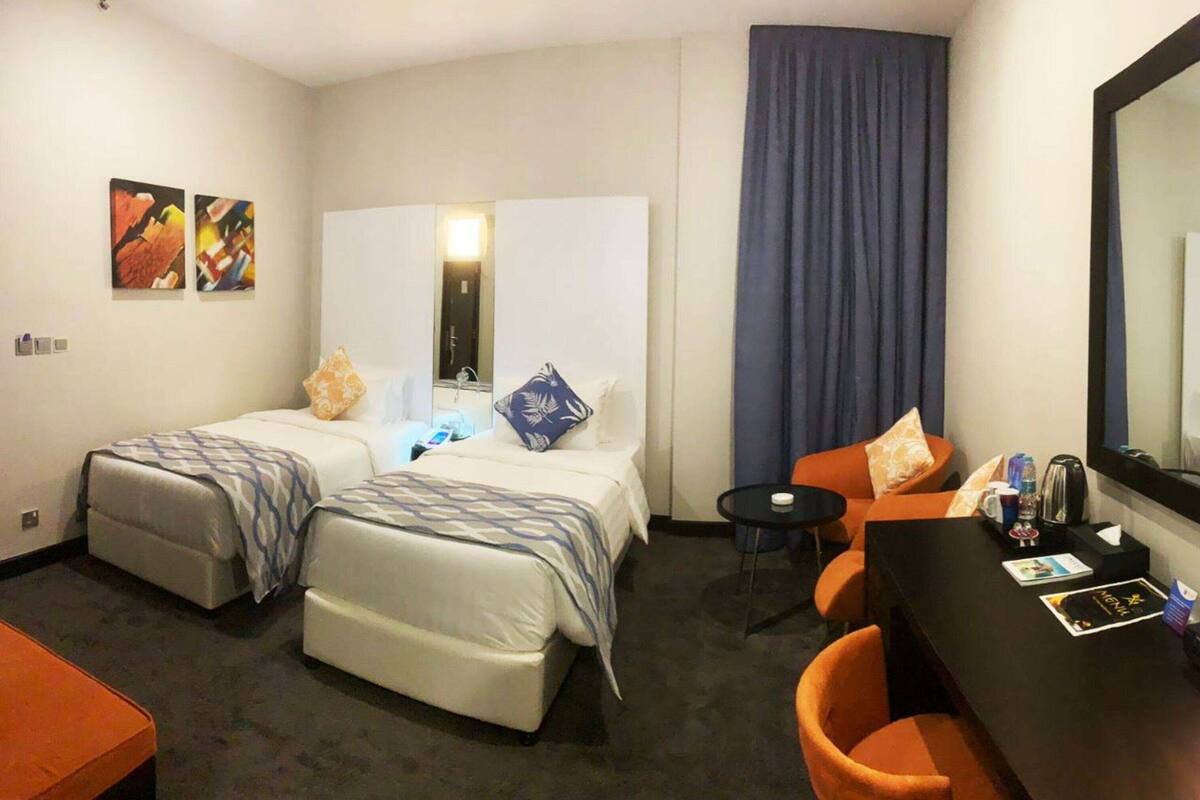 A hotel room with two beds, a desk, a chair, a small table, and a mirror.