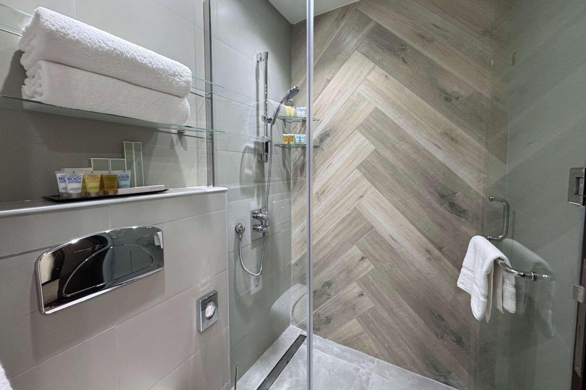 A modern bathroom with a glass shower enclosure, a vanity with a mirror, and a herringbone-patterned wall.