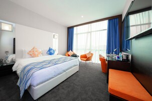 Habitación de hotel con una cama grande, un escritorio con silla, televisor y ventana con cortinas.