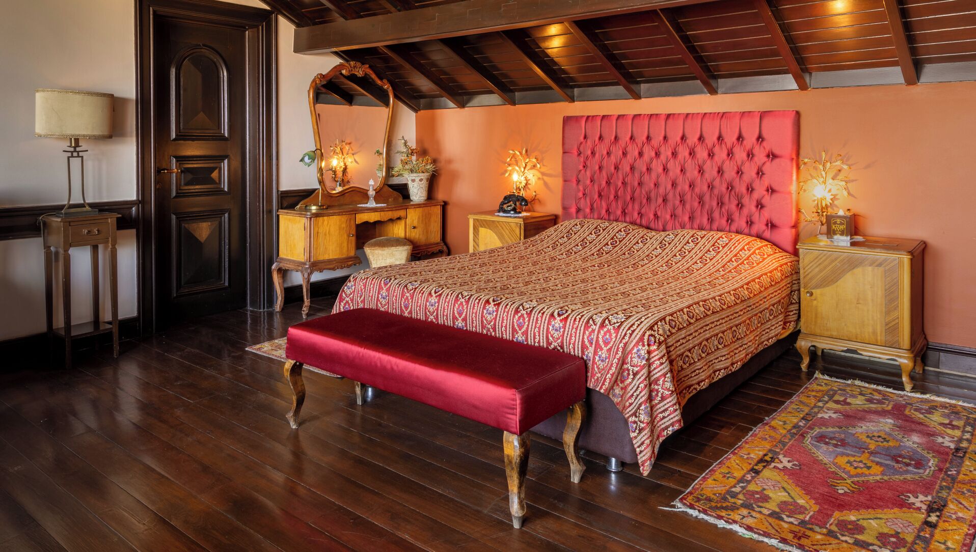 A bedroom with a large bed, a wooden bench, a dresser, a mirror, and a lamp.