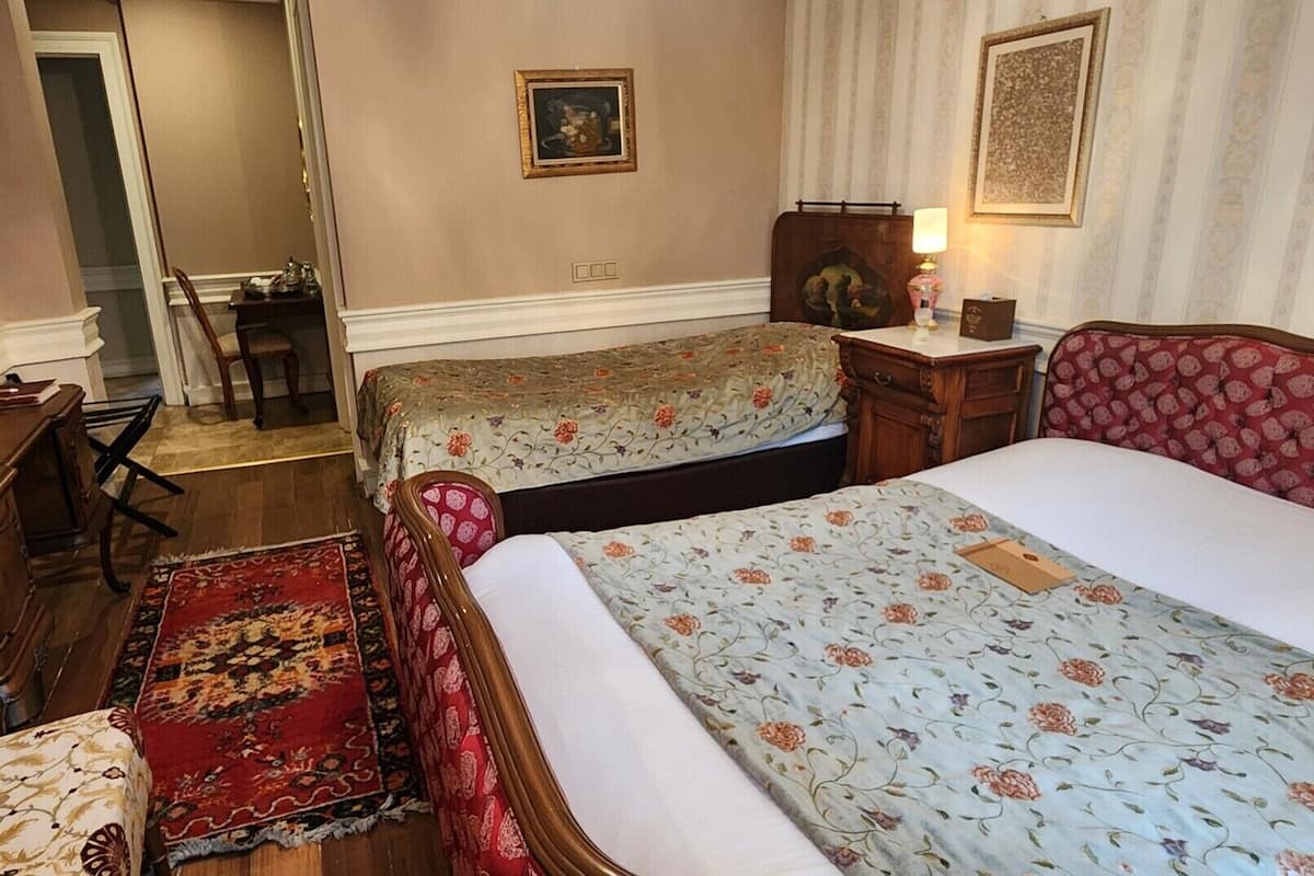 A hotel room with two beds, a desk, a chair, a small table, and a red patterned headboard.