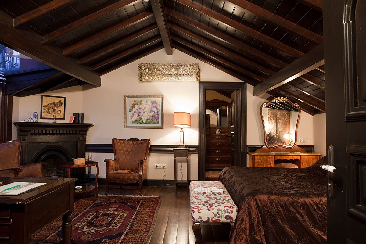 A cozy room with a fireplace, a desk, a chair, a bed, and a mirror.