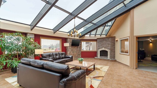A spacious living area with a high ceiling and skylight, featuring a fireplace, leather sofas, and a television. - Best Western Plus Mirage Hotel & Resort (High Level)