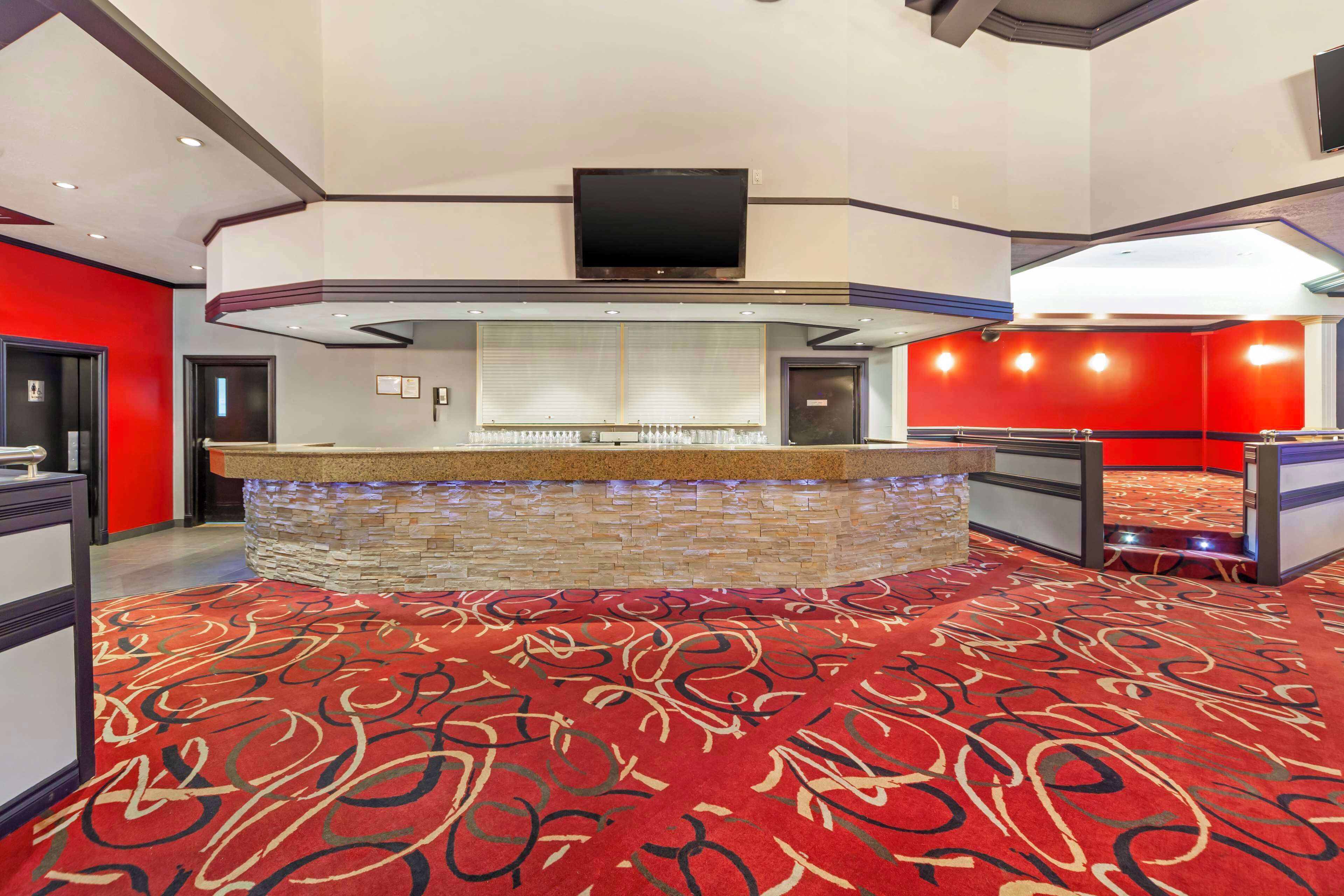 Un hall d’hôtel avec un bar en pierre, un téléviseur à écran plat fixé au-dessus, et un sol recouvert d’un tapis rouge.
