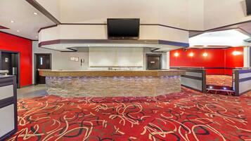 Un hall d’hôtel avec un bar en pierre, un téléviseur à écran plat fixé au-dessus, et un sol recouvert d’un tapis rouge.