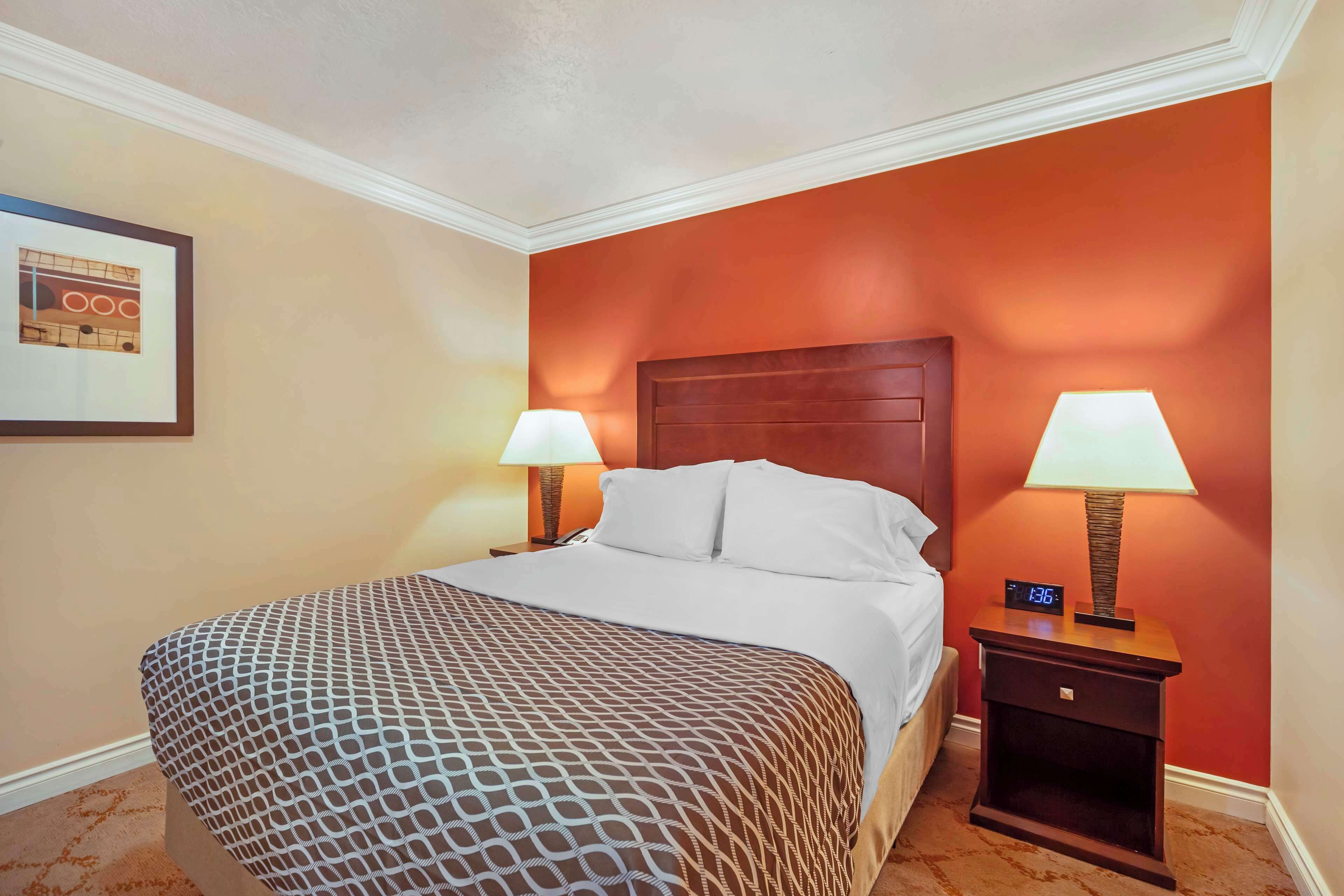 A hotel room with a large bed, two bedside lamps, a nightstand with a clock, and a framed picture on the wall.