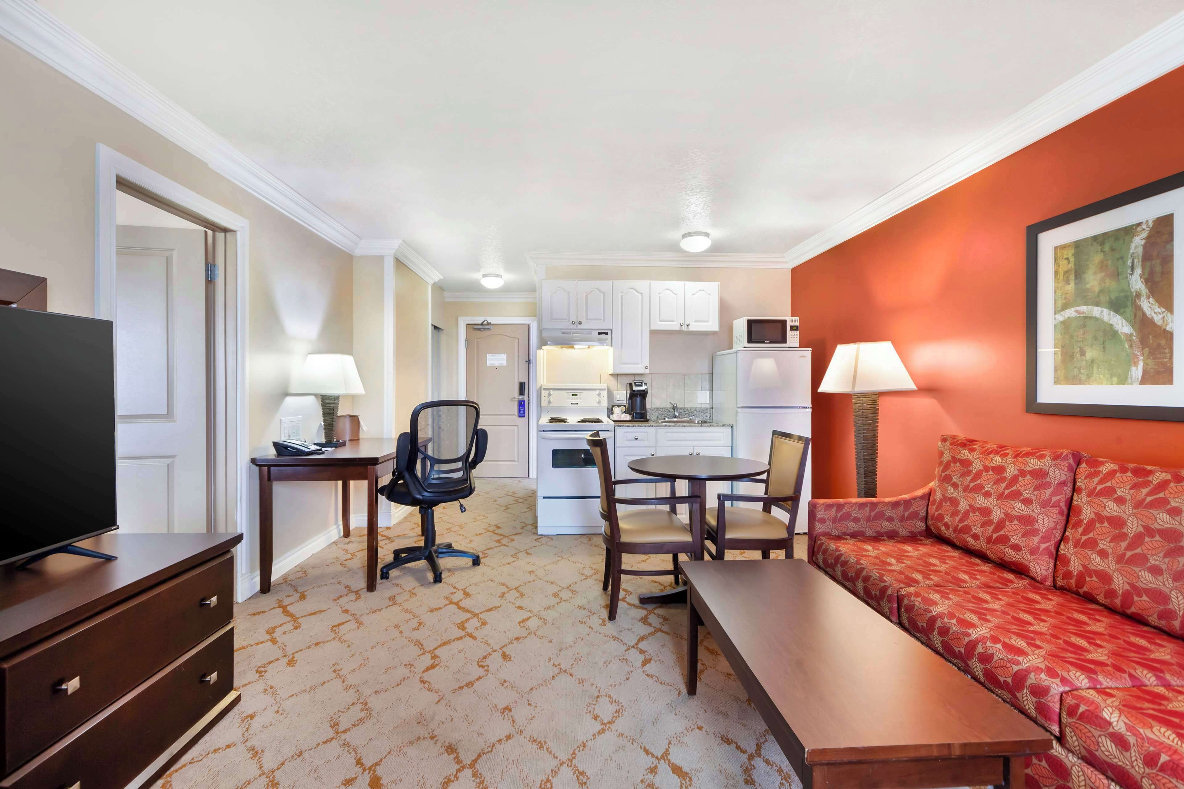 Habitación de hotel con televisor, sofá, mesa de comedor y zona de cocina.