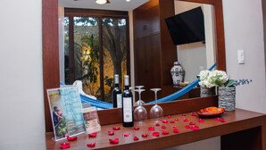 Un espace d’accueil d’hôtel avec un comptoir en bois, un miroir qui reflète la pièce, des bouteilles de vin, des verres et un vase rempli de fleurs.