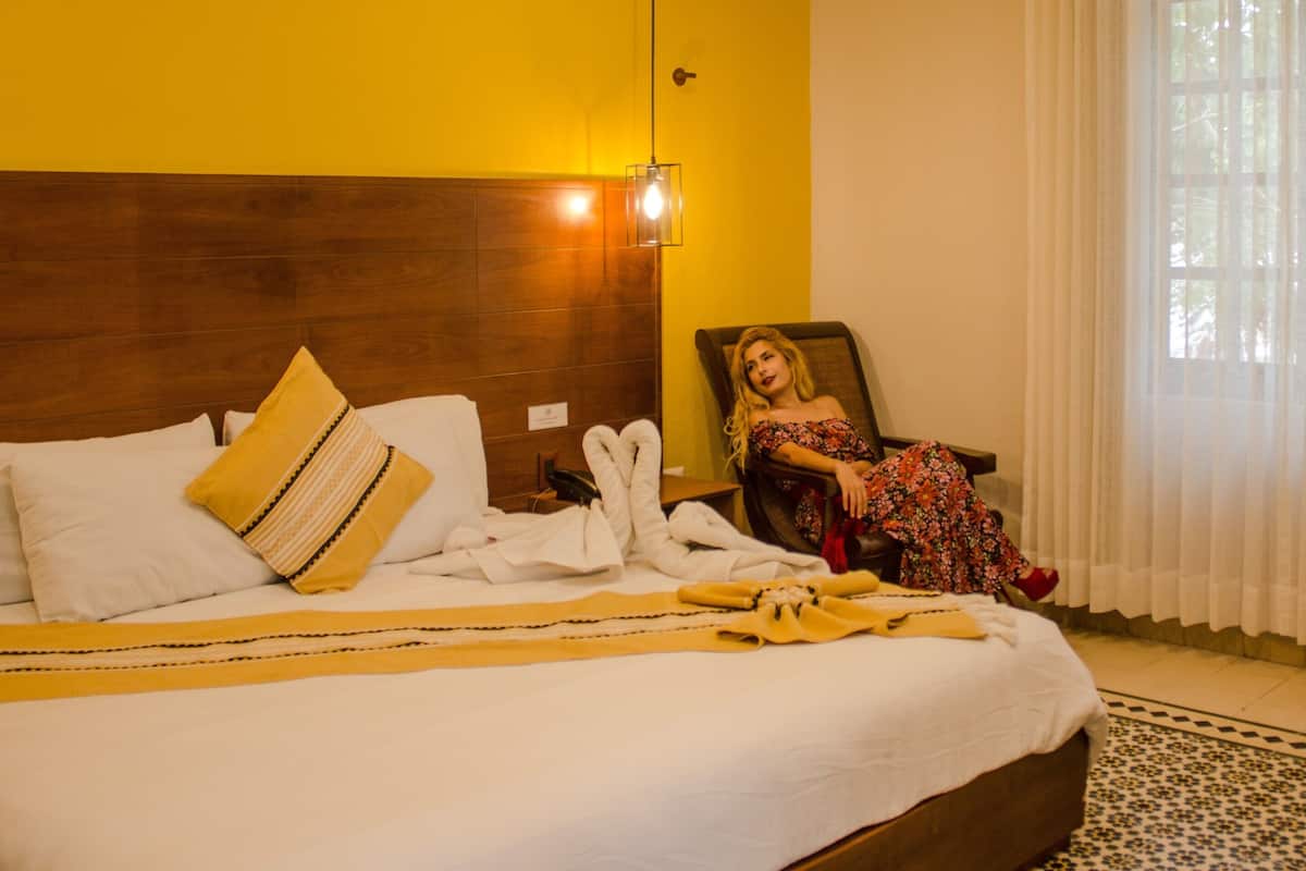 A hotel room with a large bed, a wooden headboard, a framed picture, and a window with curtains.