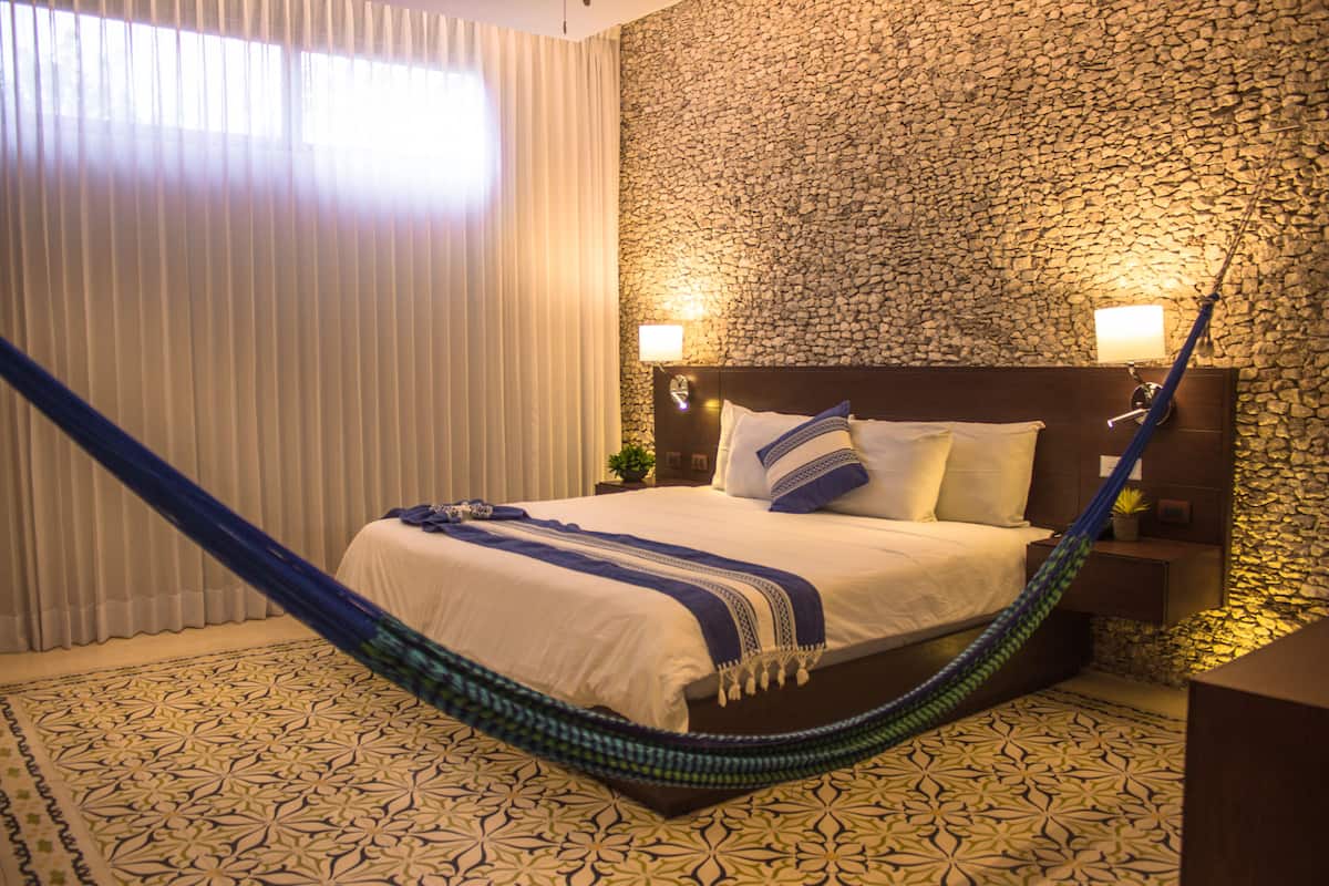 A bedroom with a bed, a hammock, a stone wall, and a patterned floor.