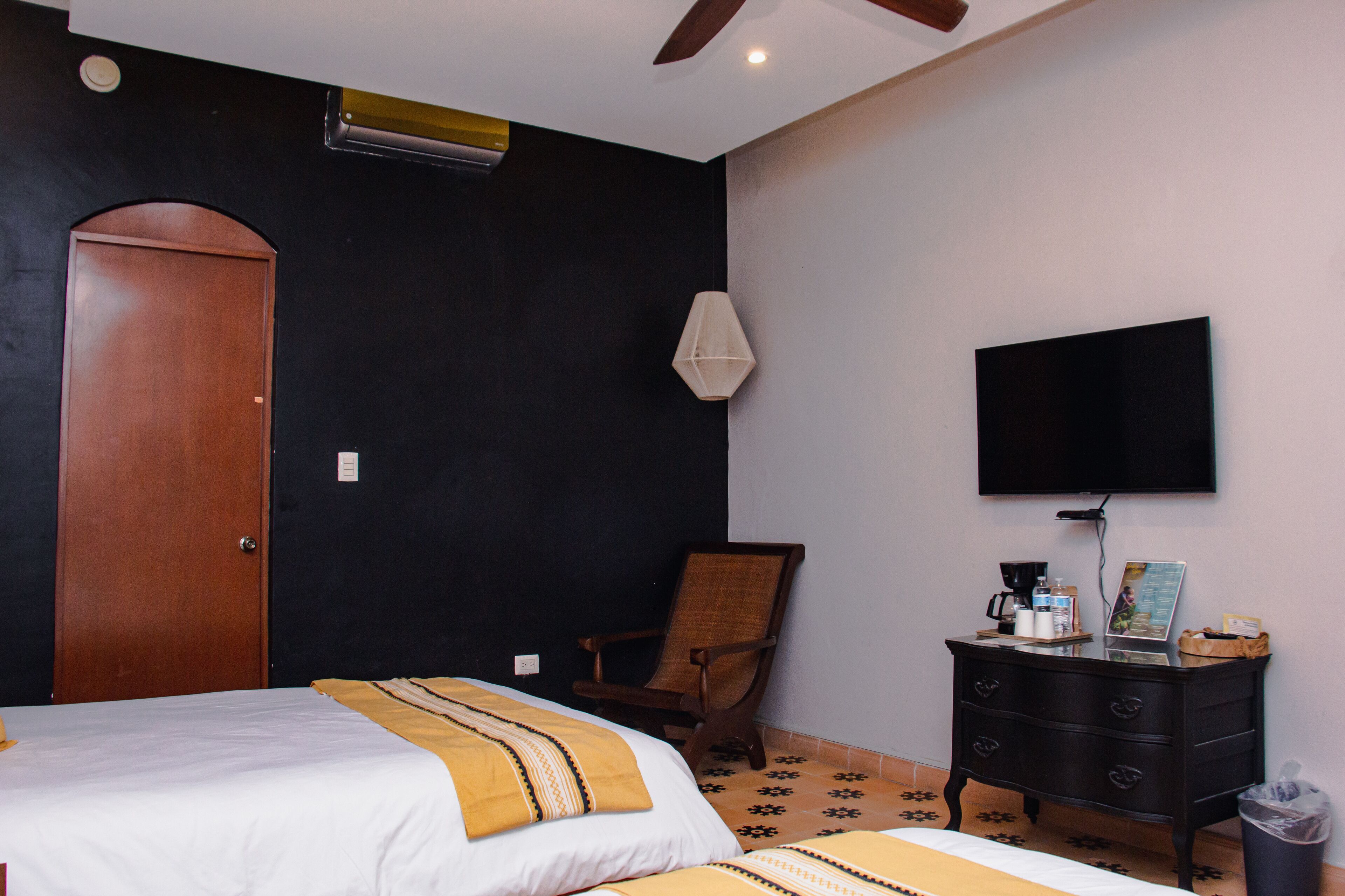 A hotel room with a bed, a wooden chair, a dresser, a television, and a door.