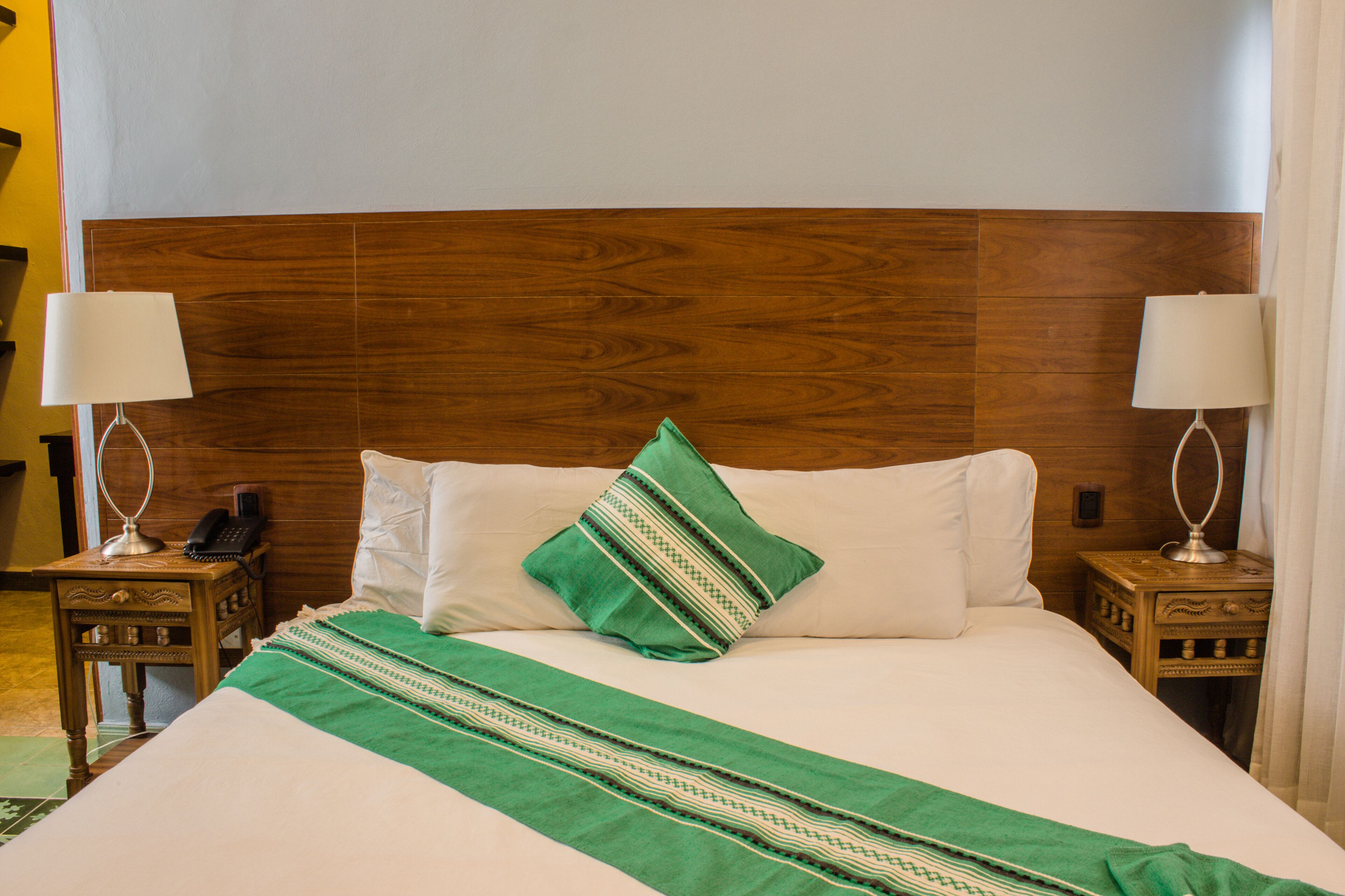 A hotel room with a wooden headboard, two bedside tables with lamps, a green throw blanket, and white bedding.