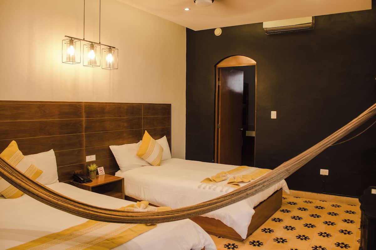 A hotel room with two beds, a wooden headboard, a hammock, a nightstand, a telephone, a plant, and a door leading to another room.