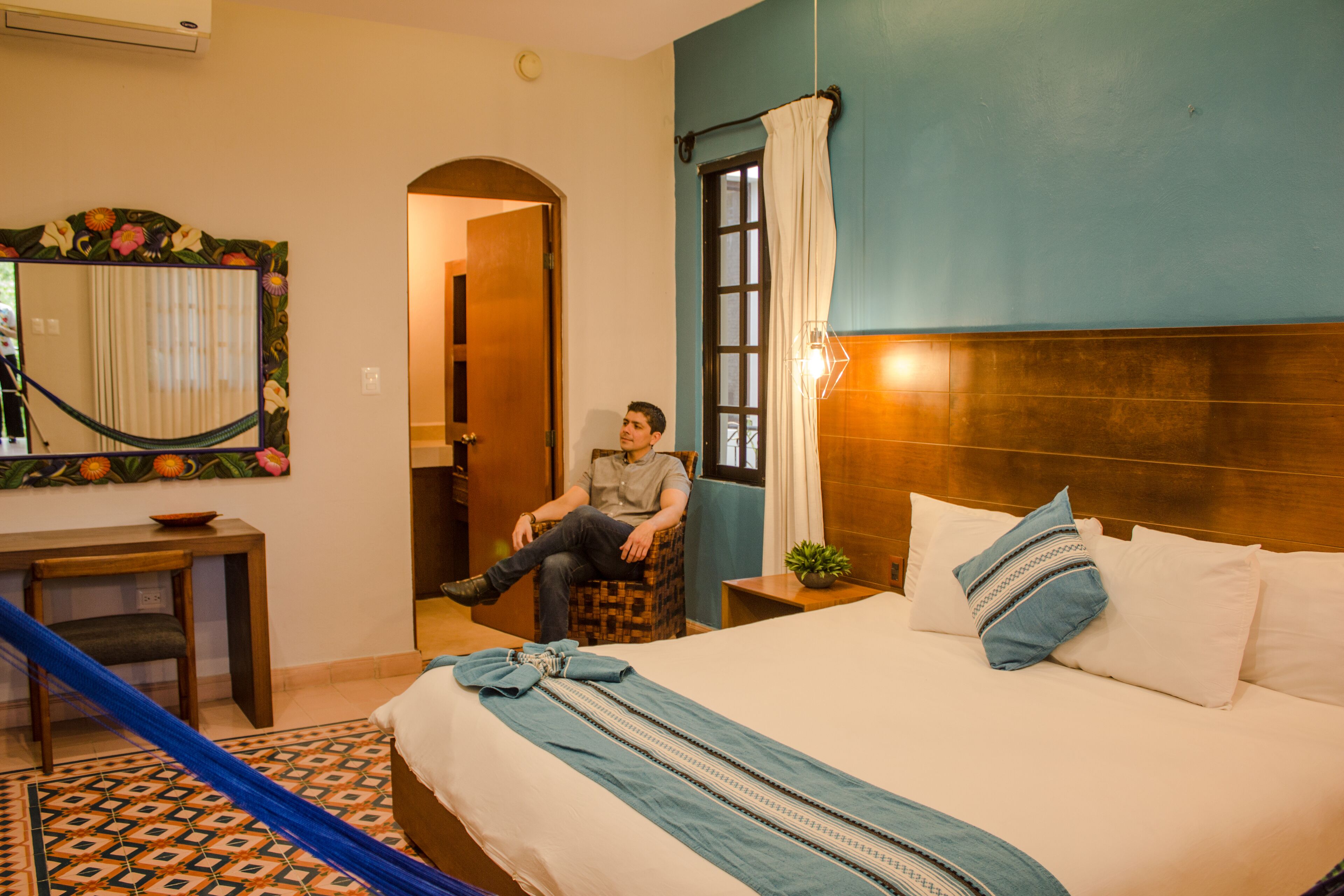 A hotel room with a bed, a chair, a desk, and a mirror.