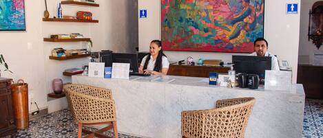 A reception desk with a marble counter, two wicker chairs, a colorful abstract painting, and a blue patterned floor.
