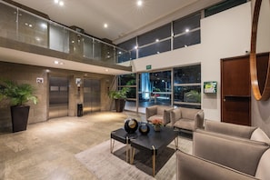 A lobby with a double-height ceiling, a reception desk, two elevators, and a seating area with chairs and a table. - Estelar Apartamentos Medellin (Medellín)