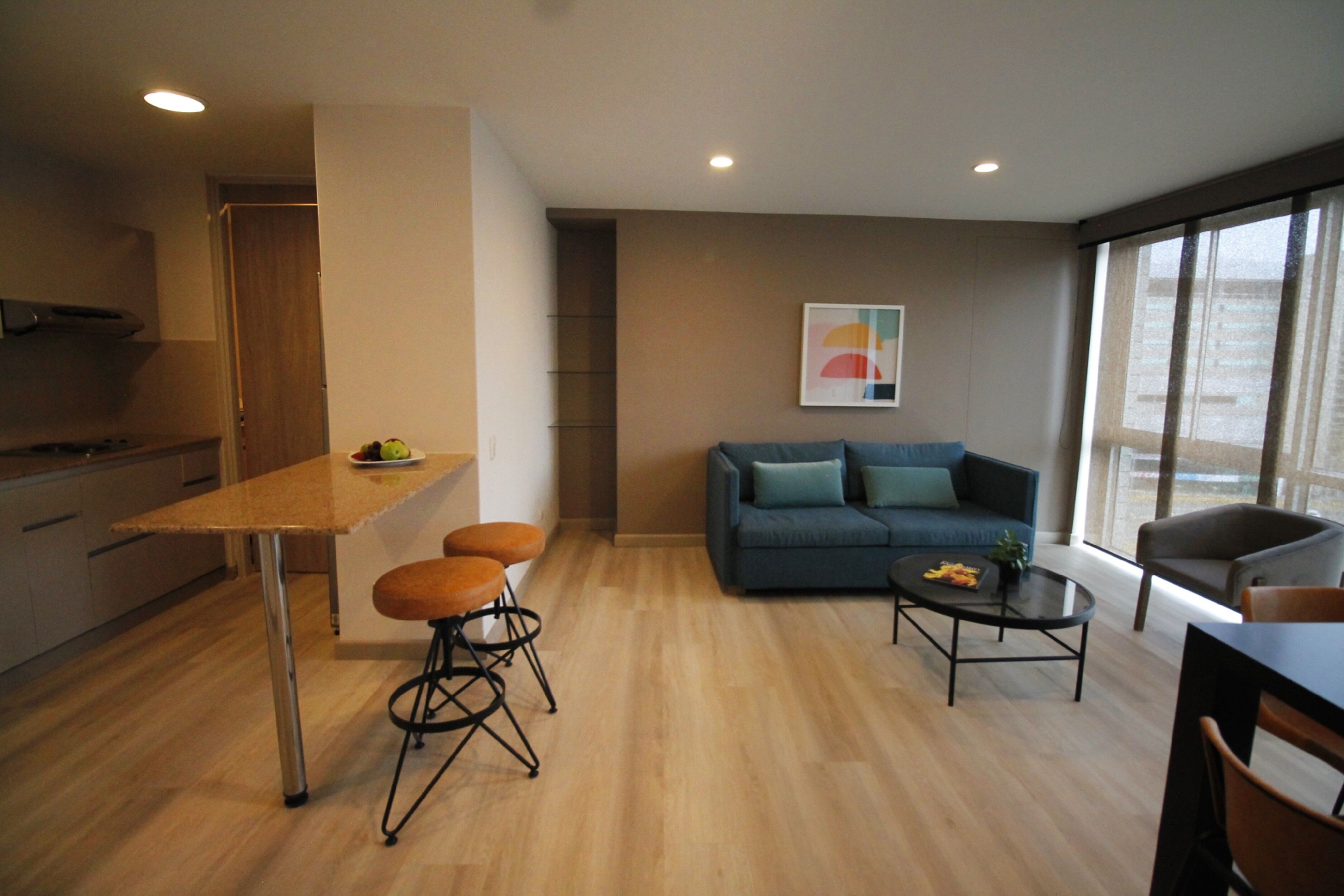 A modern living space with a kitchen area, a dining table with stools, a sofa with cushions, and a coffee table.