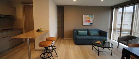 A modern living space with a kitchen area, a dining table with stools, a sofa with cushions, and a coffee table.