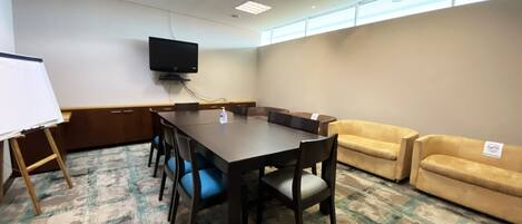 A conference room with a large table, chairs, a whiteboard, a flat-screen TV, and a sofa.