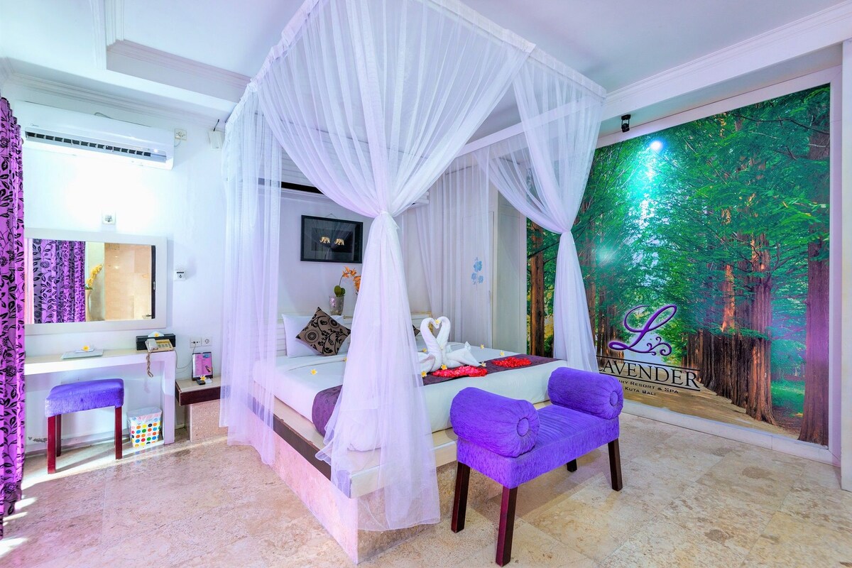 A bedroom with a four-poster bed, a desk with a chair, a purple armchair, and a forest-themed wall mural.