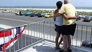 Vista de una carretera junto a la playa, con coches aparcados y una bandera.