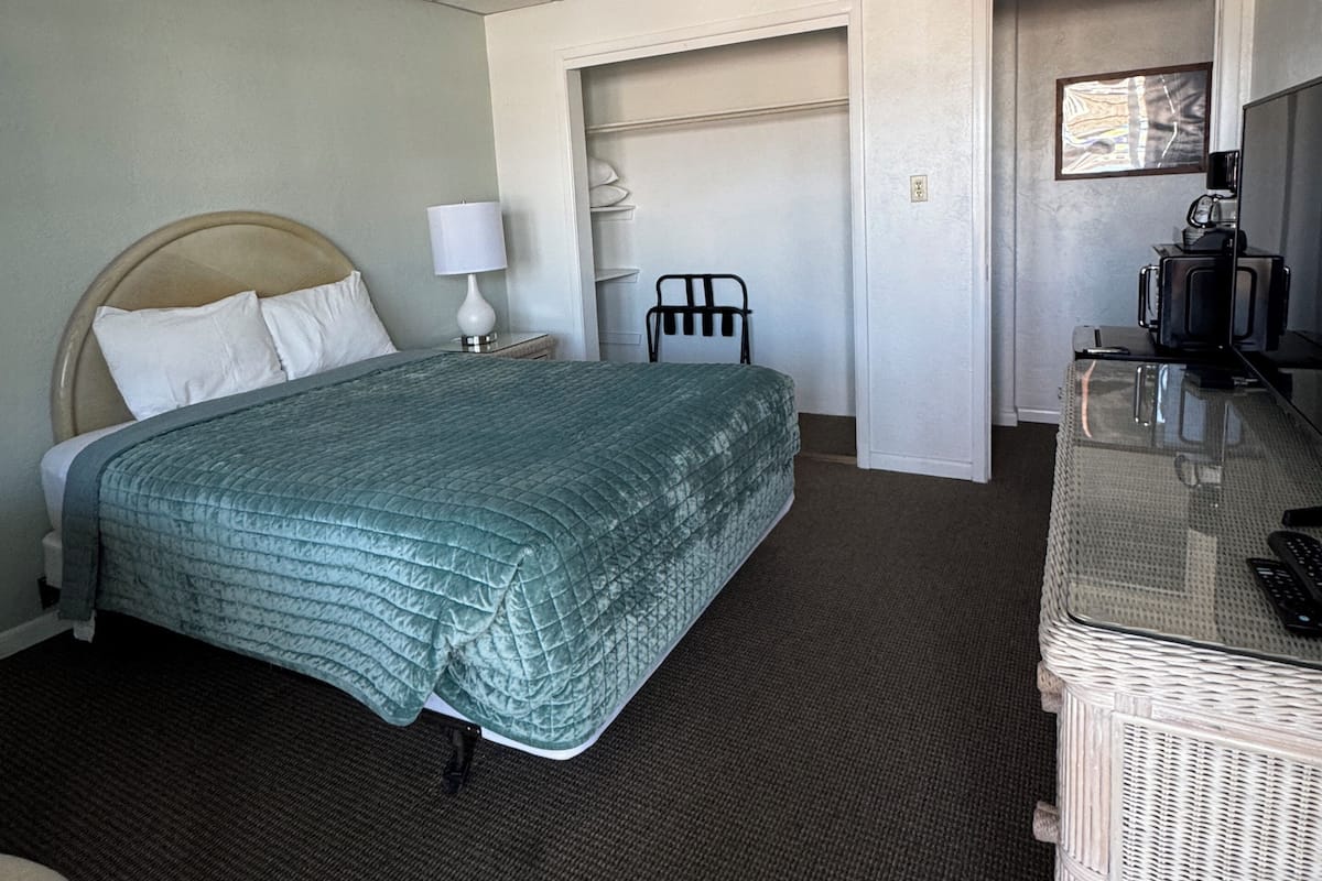 A hotel room with a bed, a desk with a computer, a chair, a lamp, and a coffee maker.