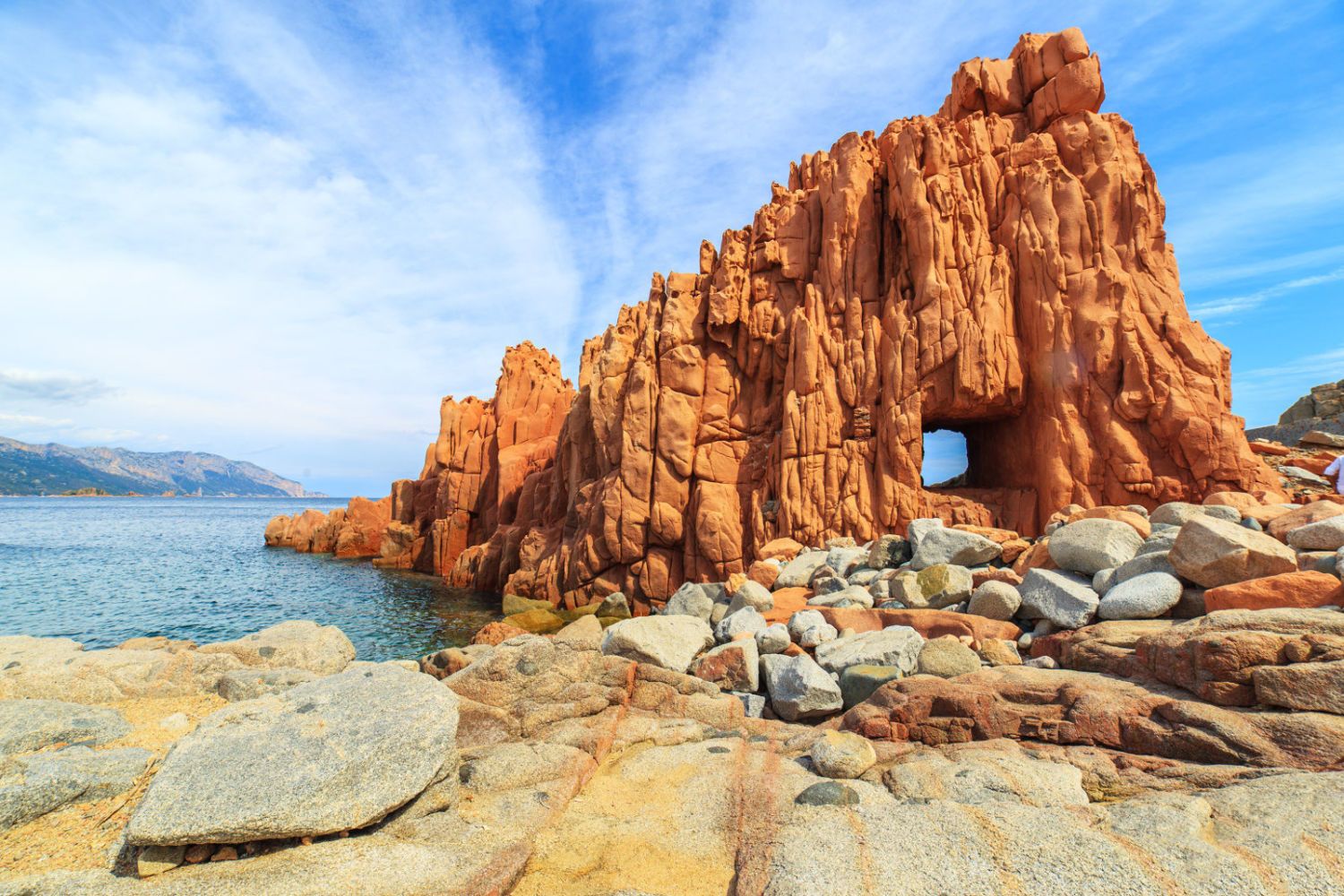 A rocky coastal landscape with a prominent rock formation featuring a natural arch.